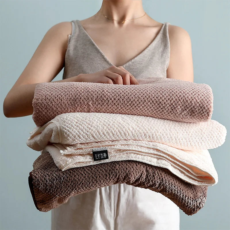 Le texte alt pour cette image serait: "Pile de serviettes de bain douces et moelleuses de différentes couleurs beige, placées dans les mains d'une personne".