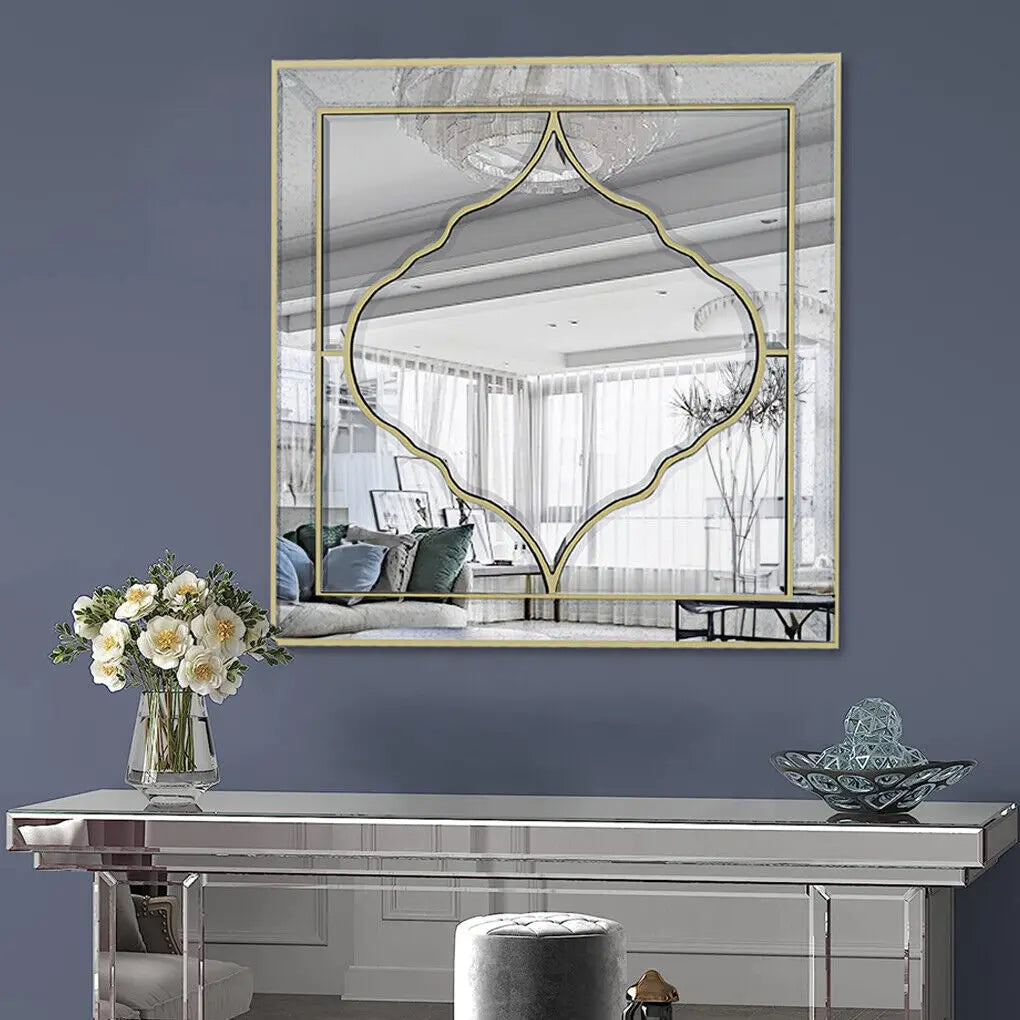 Miroir décoratif mural de style moderne avec un design géométrique doré, posé sur un meuble moderne argenté, accompagné d'un vase de fleurs blanches et d'un objet décoratif en verre, créant une atmosphère élégante et épurée dans cette pièce.