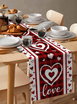 Une table dressée avec des assiettes, des verres et des pâtisseries, le tout surplombé d'un chemin de table rouge décoré de coeurs blancs et du mot "love".