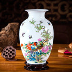 Vase décoratif en porcelaine blanche orné de fleurs colorées et d'oiseaux exotiques sur un support en bois sombre.