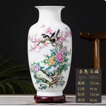 Vase décoratif en porcelaine blanche avec des motifs floraux colorés et des oiseaux, présenté sur un support en bois.