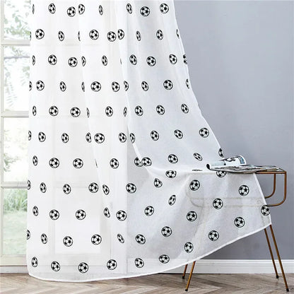 Rideaux transparents blancs avec des motifs de ballons de football noirs, tombant avec fluidité sur le sol près d’une table dorée.