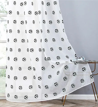 Rideaux transparents blancs avec des motifs de ballons de football noirs, tombant avec fluidité sur le sol près d’une table dorée.