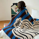 Une personne enveloppée dans une couverture bleue et blanche avec un motif impressionnant de tigre, assise près d'une armoire et d'un lit.