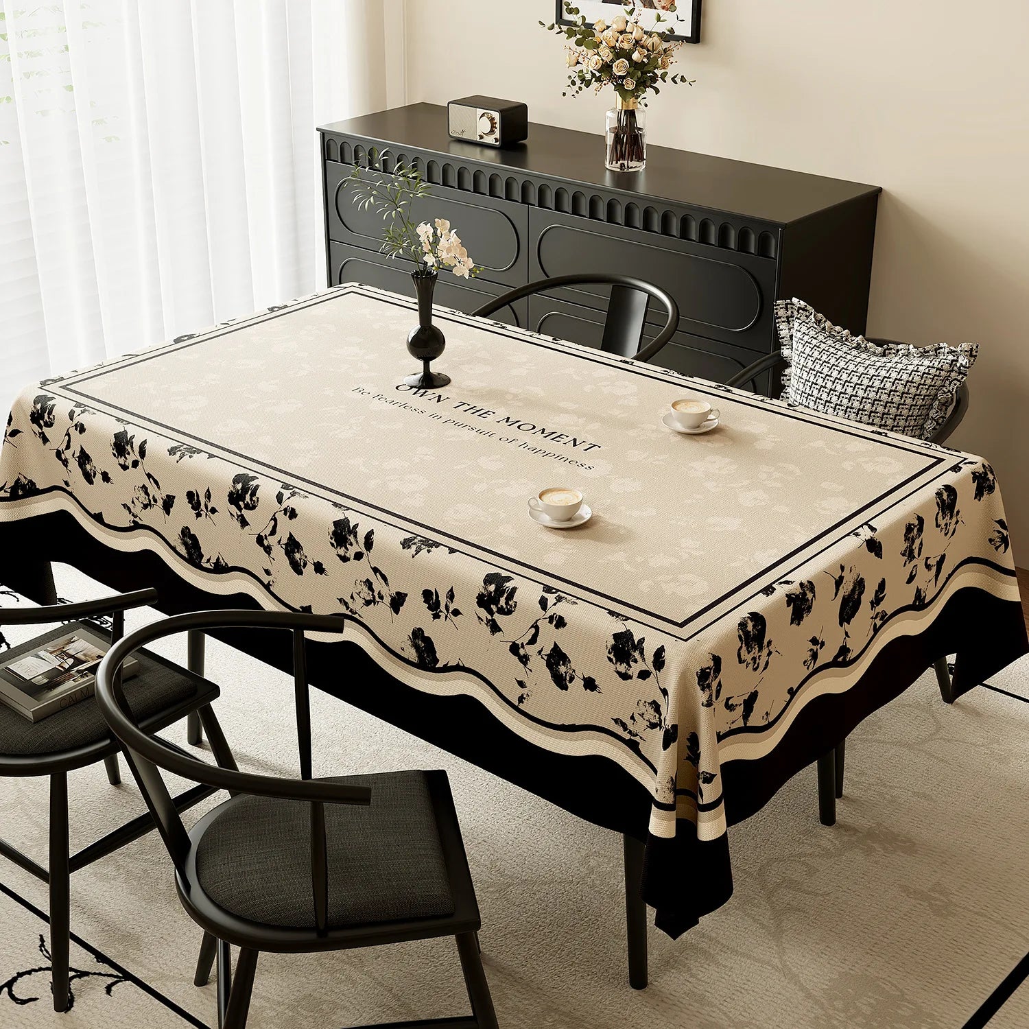 Une décoration élégante et chaleureuse, avec une table aux motifs fleuris, un meuble noir et un arrangement floral sur le côté.