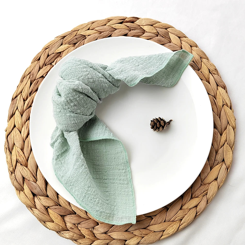 Un plat en céramique blanche posé sur un dessous-de-plat tressé en fibres naturelles, avec un élégant linge de table vert pastel et un cône de pin.