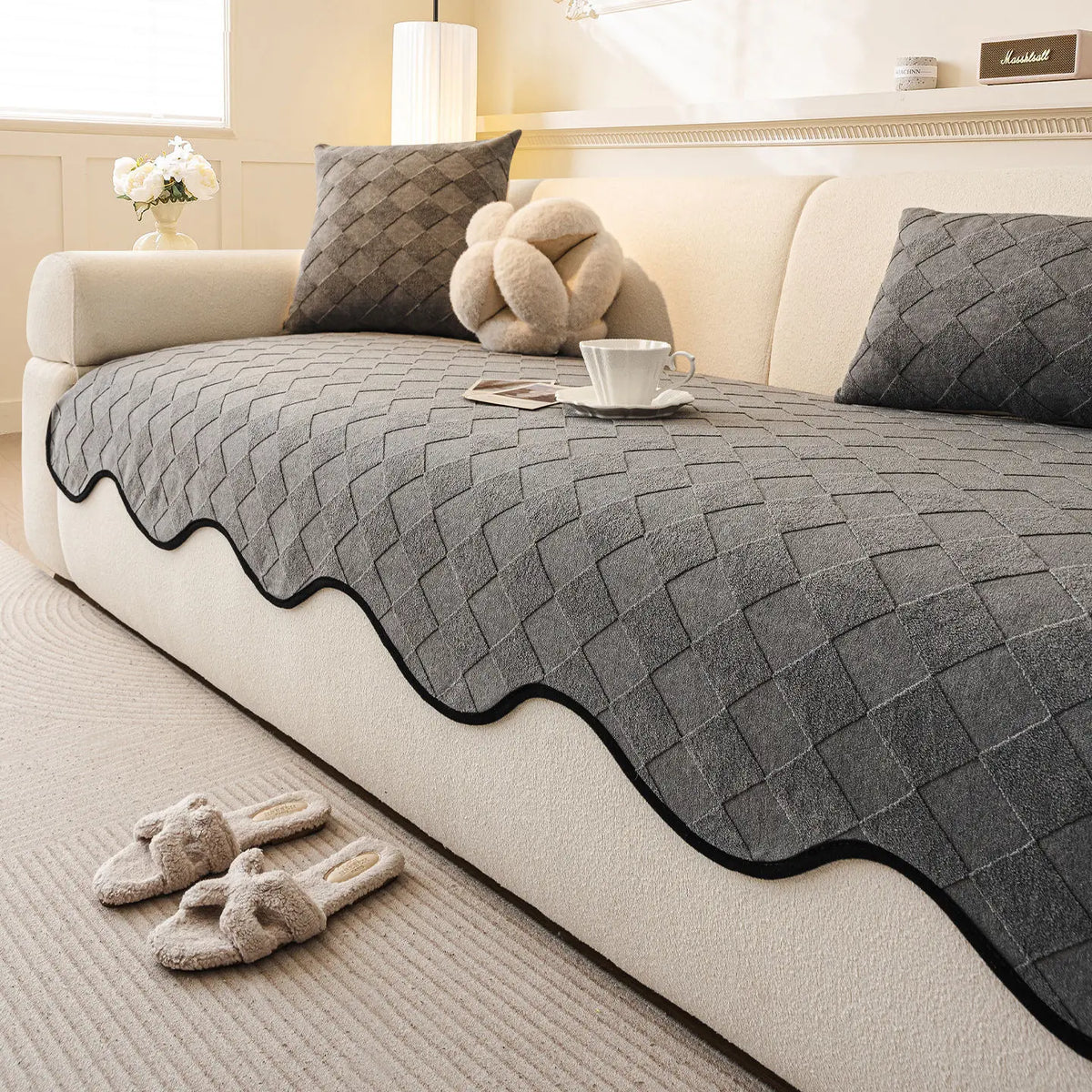 Coussins et couverture en gris foncé sur un canapé beige, avec tasse de café et décorations.