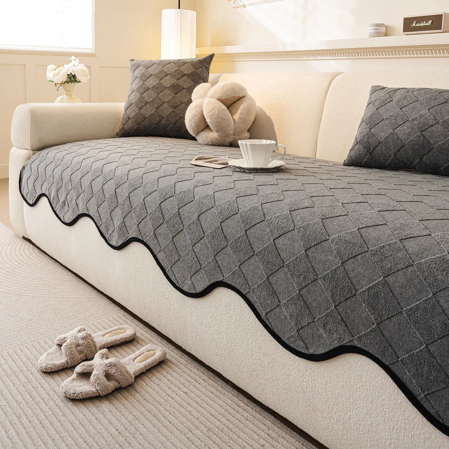 Coussins et couverture en gris foncé sur un canapé beige, avec tasse de café et décorations.