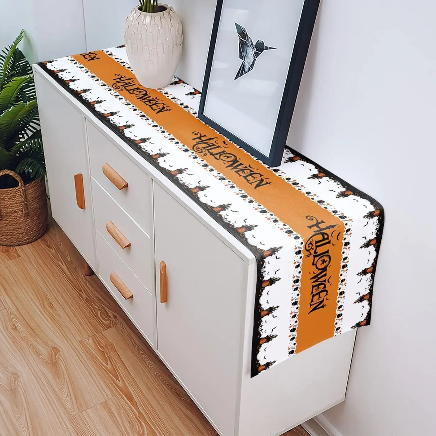 Le meuble blanc avec des rangements et un chemin de table orange aux motifs noirs crée une atmosphère chaleureuse et contemporaine dans cette pièce décorée avec soin.