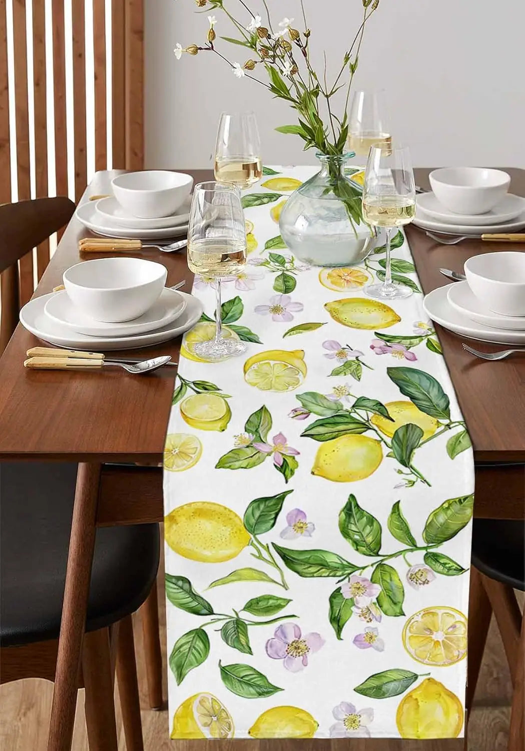 Le texte alt pour cette image serait : Superbe arrangement de table avec des fleurs, des citrons, des verres de vin et de la vaisselle blanche sur un chemin de table au motif florale aux couleurs ensoleillées.
