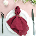 Une nappe blanche avec des fleurs blanches et une serviette en tissu bordeaux roulée et attachée avec une ficelle sur une assiette blanche.