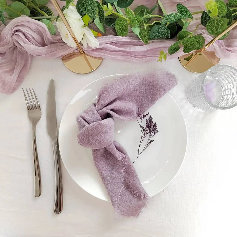 Une table élégante avec des couverts dorés, une serviette de table violette et des fleurs vertes décorant une assiette blanche.