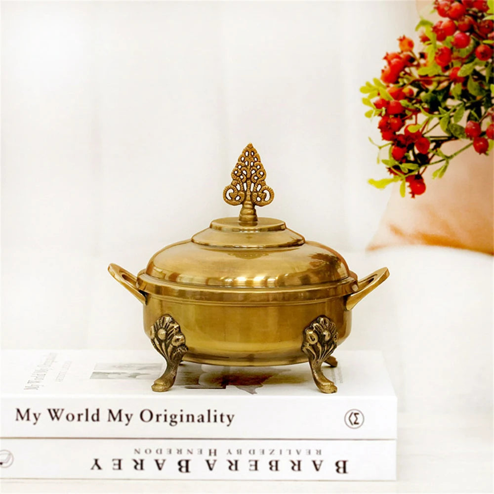 Coupe métallique dorée avec un élégant motif ciselé, posée sur une surface blanche à côté d'une décoration florale aux couleurs vives.