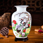 Un vase décoratif en porcelaine blanche orné de motifs de grues, de fleurs et de branches de cerisier en fleurs.