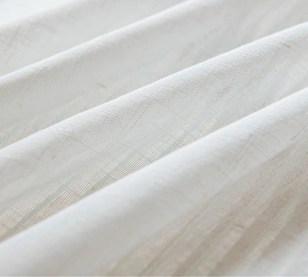 Vue rapprochée des plis du tissu blanc fin et texturé du voilage.
