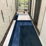 Le couloir moderne est décoré avec un motif géométrique bleu et gris sur le sol, reflétant la lumière naturelle qui entre par les grandes baies vitrées.