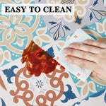 Tapis ou tapisserie motifs floraux et damassés sur fond beige et bleu, avec une main essuyant une tache rouge, accompagné du texte "EASY TO CLEAN" indiquant que le produit est facile à nettoyer.