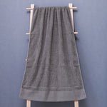 Serviette de bain en coton gris suspendue sur un support en bois.