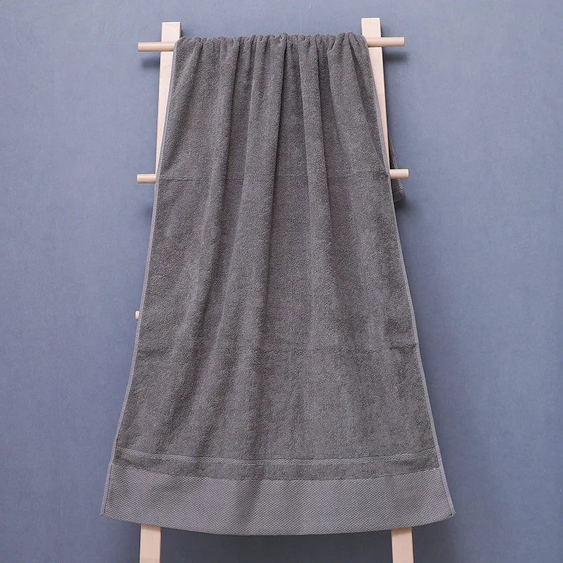 Serviette de bain en coton gris suspendue sur un support en bois.