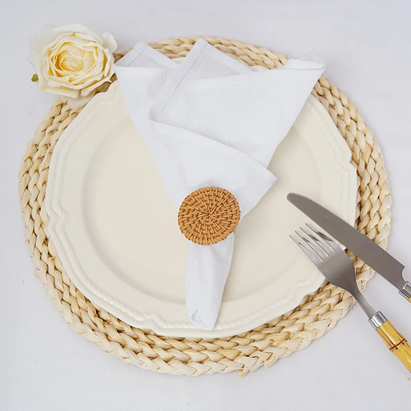 Composition élégante avec une assiette blanche, des couverts et une fleur sur un dessous de plat en osier tressé.