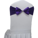 Une élégante chaise blanche ornée d'un nœud papillon violet foncé, prête à accueillir un invité pour un événement spécial.