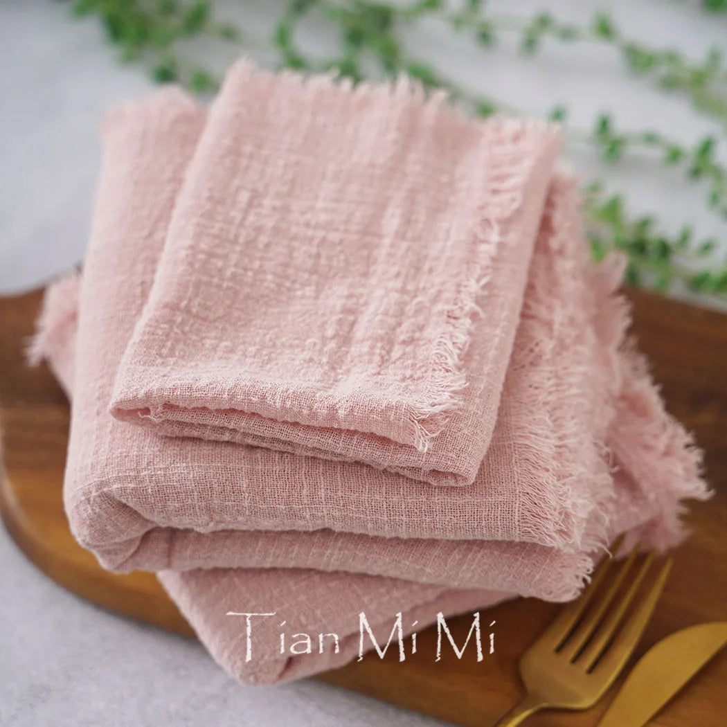 Une pile de serviettes en lin rose posée sur un plat en bois, avec des couverts dorés à côté, créant une atmosphère élégante et chaleureuse.