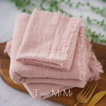 Une pile de serviettes en lin rose posée sur un plat en bois, avec des couverts dorés à côté, créant une atmosphère élégante et chaleureuse.