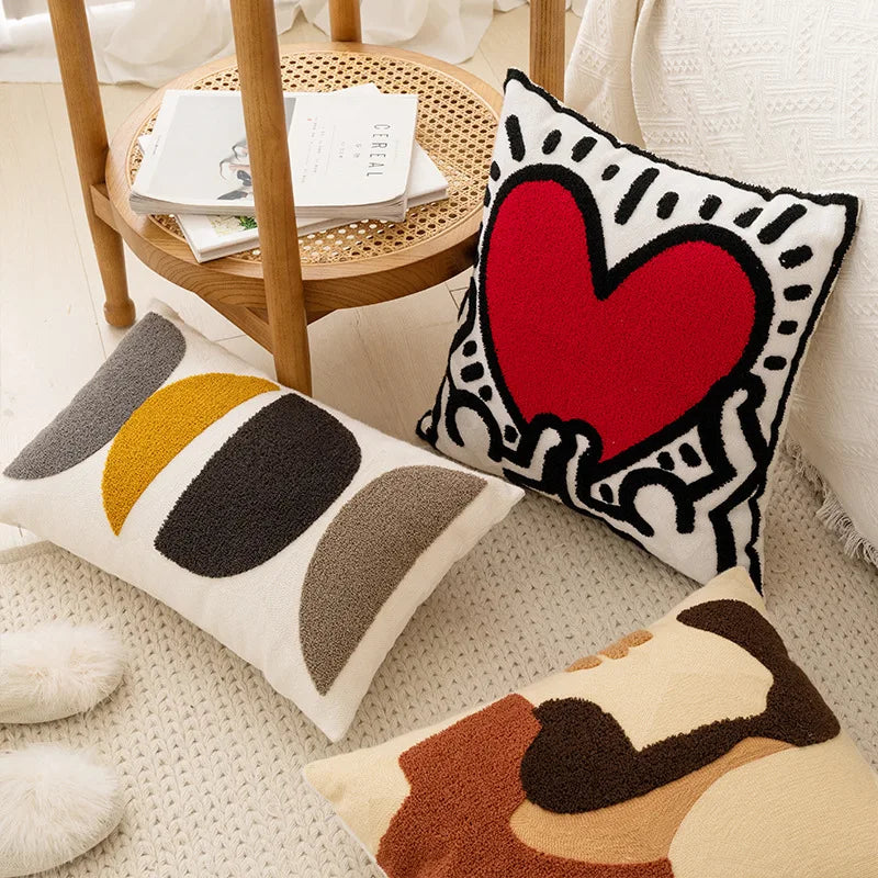 Des coussins décoratifs avec des motifs géométriques et un grand cœur rouge sur une table basse en bois.