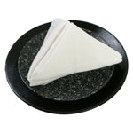 Serviette blanche pliée sur une assiette noire avec motif en granit.