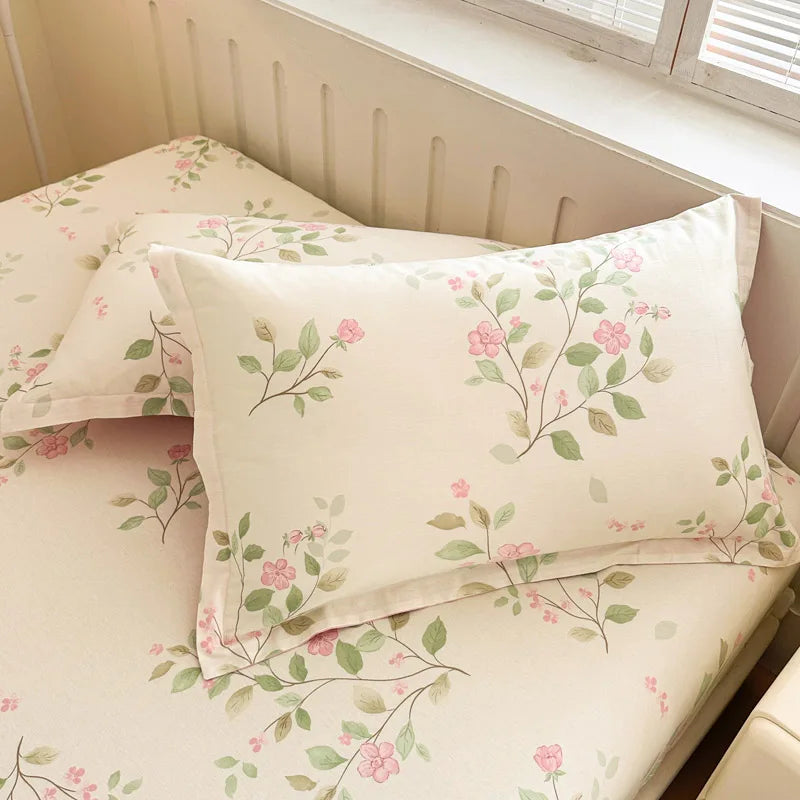 Des draps de lit en coton fleuri pastel, avec des motifs de fleurs roses et de feuilles vertes sur un fond crème, créant une ambiance douce et sereine.
