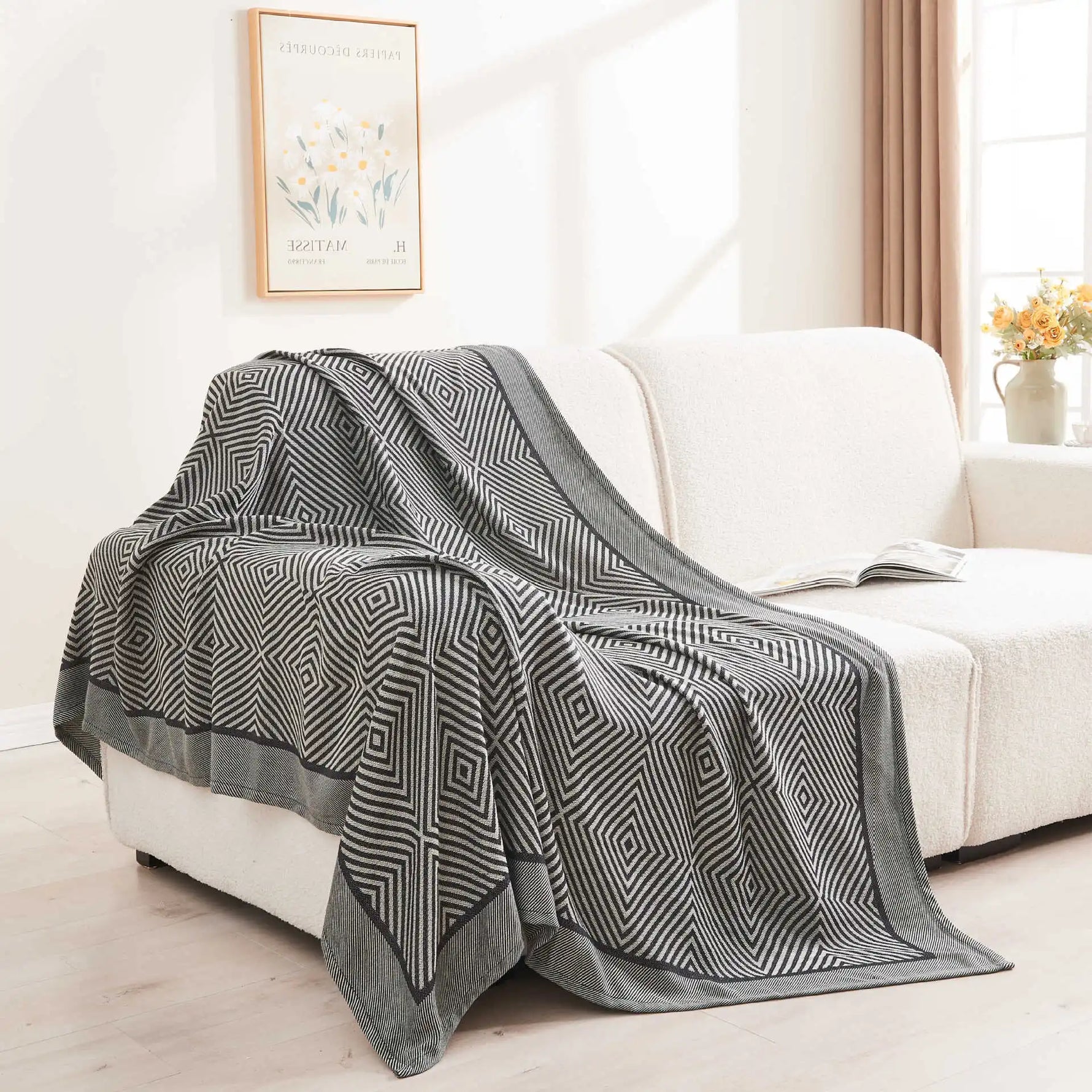 Une couverture confortable à motifs géométriques noirs et blancs repose sur un canapé, accompagnée d'un livre posé à côté.