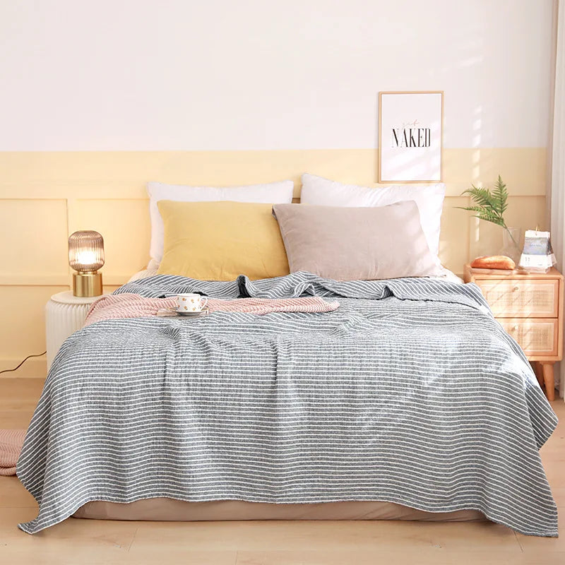 Une chambre à coucher élégante avec un lit double, une couverture rayée grise et blanche, des oreillers beiges et une décoration de style scandinave.