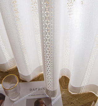Voilage blanc à ruflette prêt à poser avec broderies délicates, lumière filtrée dans un salon élégant.
