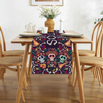 Nappe décorative multicolore avec imprimé de crânes de Calavera et autres motifs mexicains traditionnels sur une table de salle à manger en bois avec des chaises.