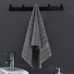 Un élégant porte-serviette noir suspendu au mur, avec un ample et moelleux essuie-main gris rayé, créant une atmosphère sophistiquée et apaisante dans cette salle de bain.