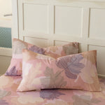 Des oreillers décoratifs aux motifs de feuilles tropicales roses et violettes, créant une ambiance chaleureuse et apaisante dans la chambre.