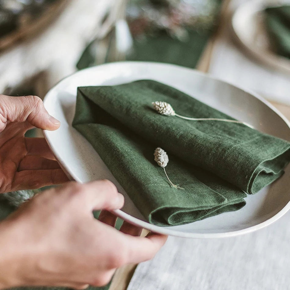 Deux mains disposent délicatement une étoffe verte sur une assiette blanche, avec quelques petites fleurs blanches posées délicatement sur le tissu.