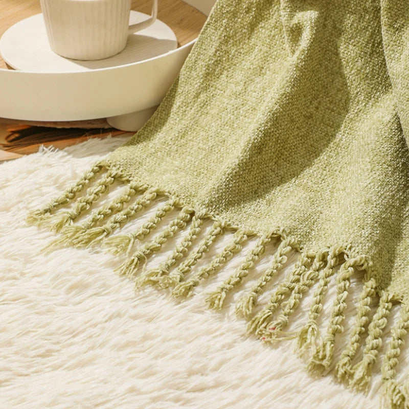 Une couverture en tricot vert anis avec des pompons décoratifs.