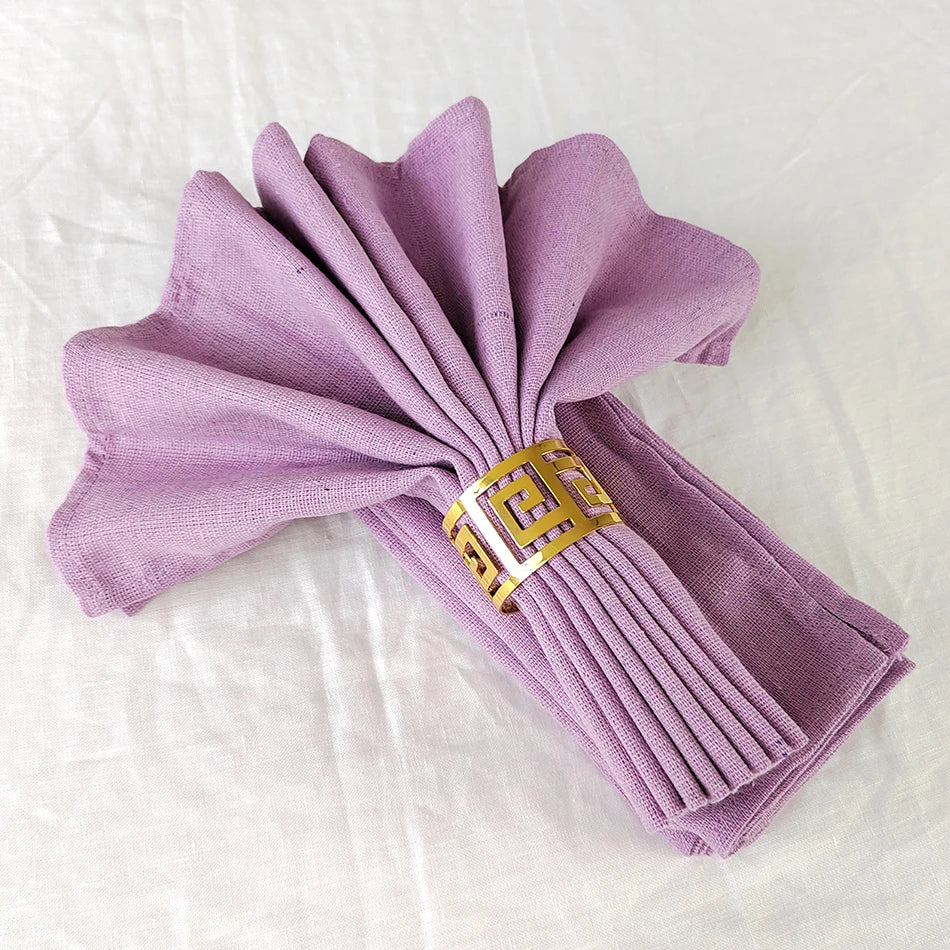 Cette image montre un éventail de serviettes de table en tissu violet, pliées avec élégance et maintenues ensemble par un anneau décoratif en métal doré.