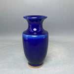 Vase en céramique bleu foncé avec une forme caractéristique et un aspect brillant.