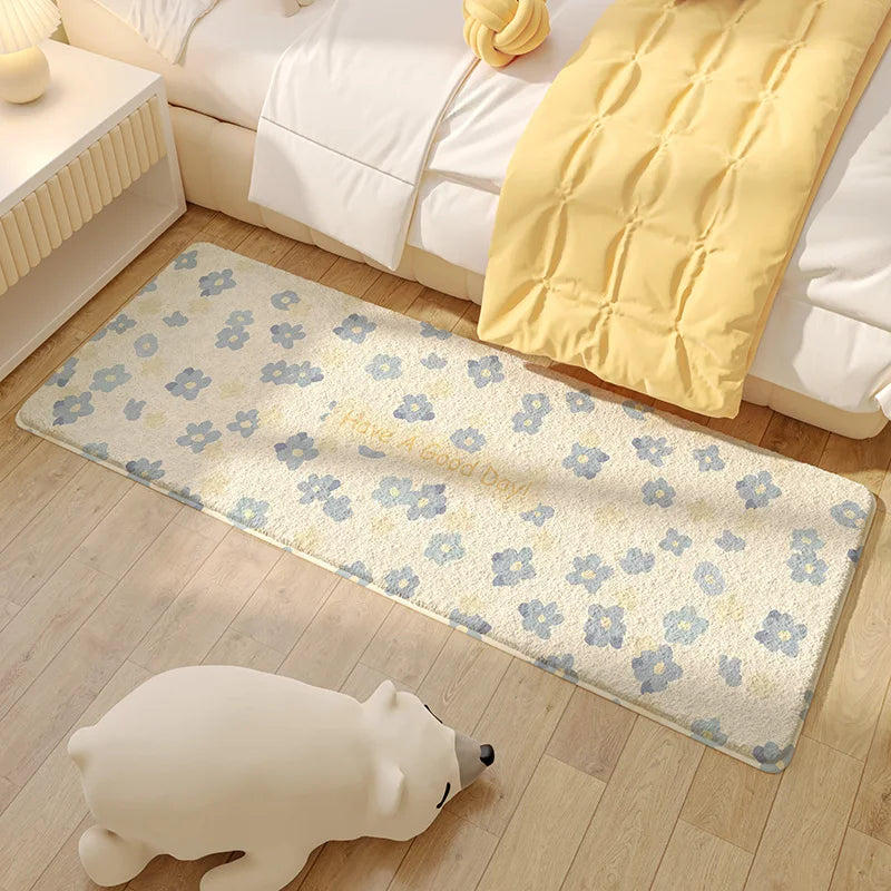 Un tapis de sol à motifs floraux bleus posé sur un parquet clair dans une chambre chaleureuse aux draps et couvertures jaunes.