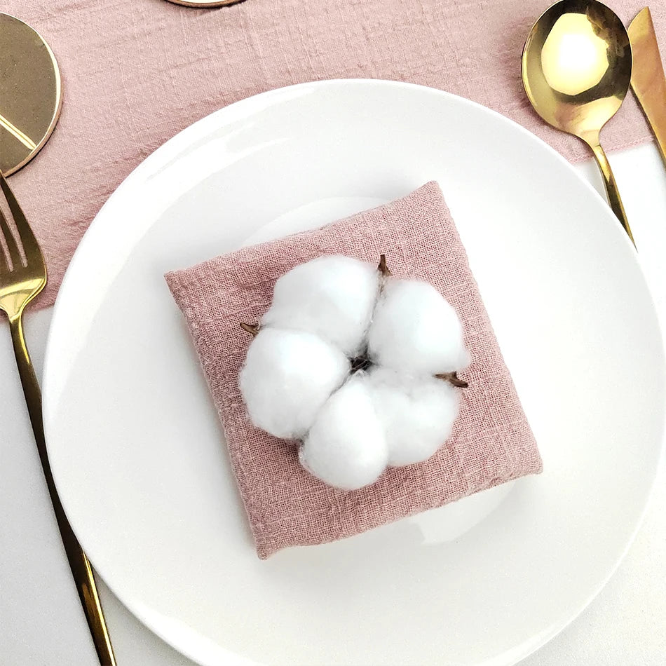 Un beau bouquet de coton blanc disposé élégamment sur un linge rose pâle, entouré d'ustensiles de cuisine dorés.