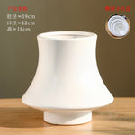 Ce vase en céramique blanche mat a une forme unique avec un profil épanoui. Ses dimensions sont d'environ 19 cm de diamètre, 12 cm de largeur et 18 cm de hauteur, ce qui en fait un objet décoratif de taille moyenne.