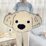 Une grande et moelleuse peluche de chien de type Golden Retriever, dans des tons gris et beige, est tenue devant une fenêtre par une personne vêtue d'un sweat-shirt gris avec le texte "Newport".