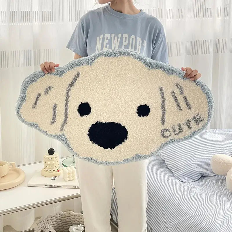Une grande et moelleuse peluche de chien de type Golden Retriever, dans des tons gris et beige, est tenue devant une fenêtre par une personne vêtue d'un sweat-shirt gris avec le texte "Newport".