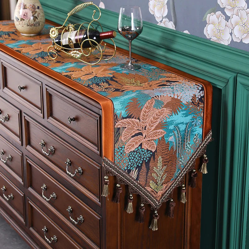 La photo montre une commode en bois avec un chemin de table motif tropical coloré, décoré d'une bouteille de vin et d'un verre à vin posés sur le dessus.