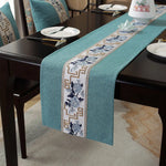Cette image montre un chemin de table vert décoré de motifs floraux et géométriques, posé sur une table avec des accessoires de table.