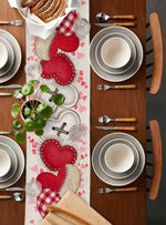 Une table dressée élégamment avec des assiettes et des ustensiles, ornée de motifs de coeurs rouges et de napperons à carreaux.