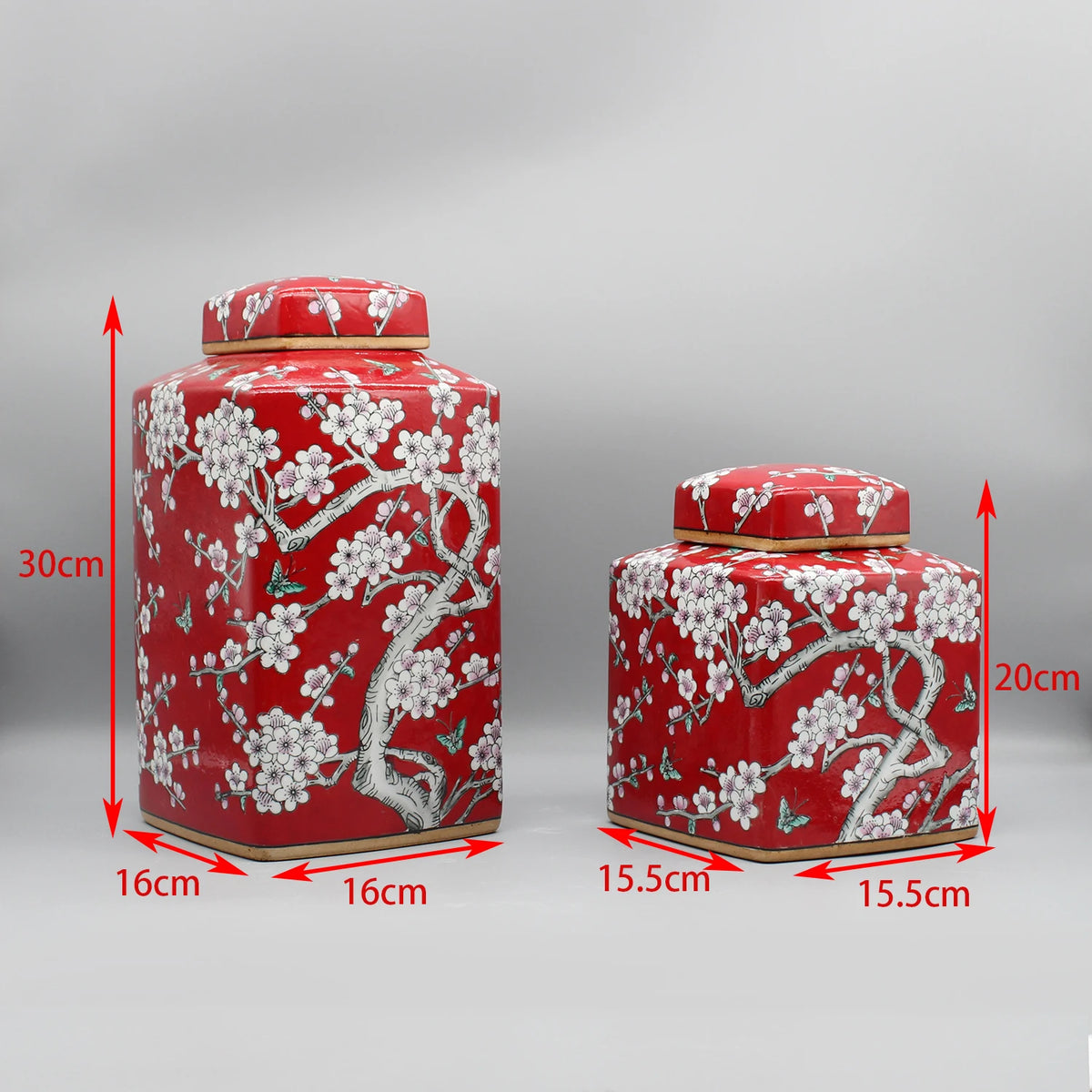 Deux élégants récipients cylindriques rouges décorés de motifs floraux blancs dans un style oriental, présentant des dimensions et des tailles distinctes.