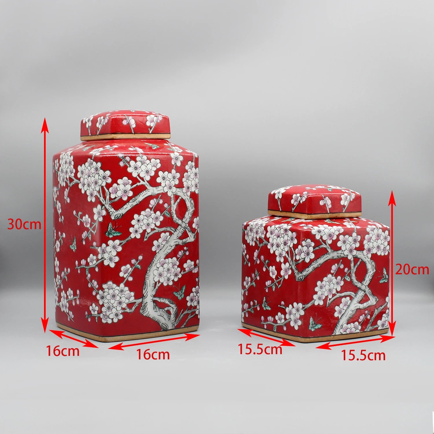 Deux élégants récipients cylindriques rouges décorés de motifs floraux blancs dans un style oriental, présentant des dimensions et des tailles distinctes.